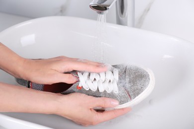 Photo of Woman washing sport shoe in sink, closeup