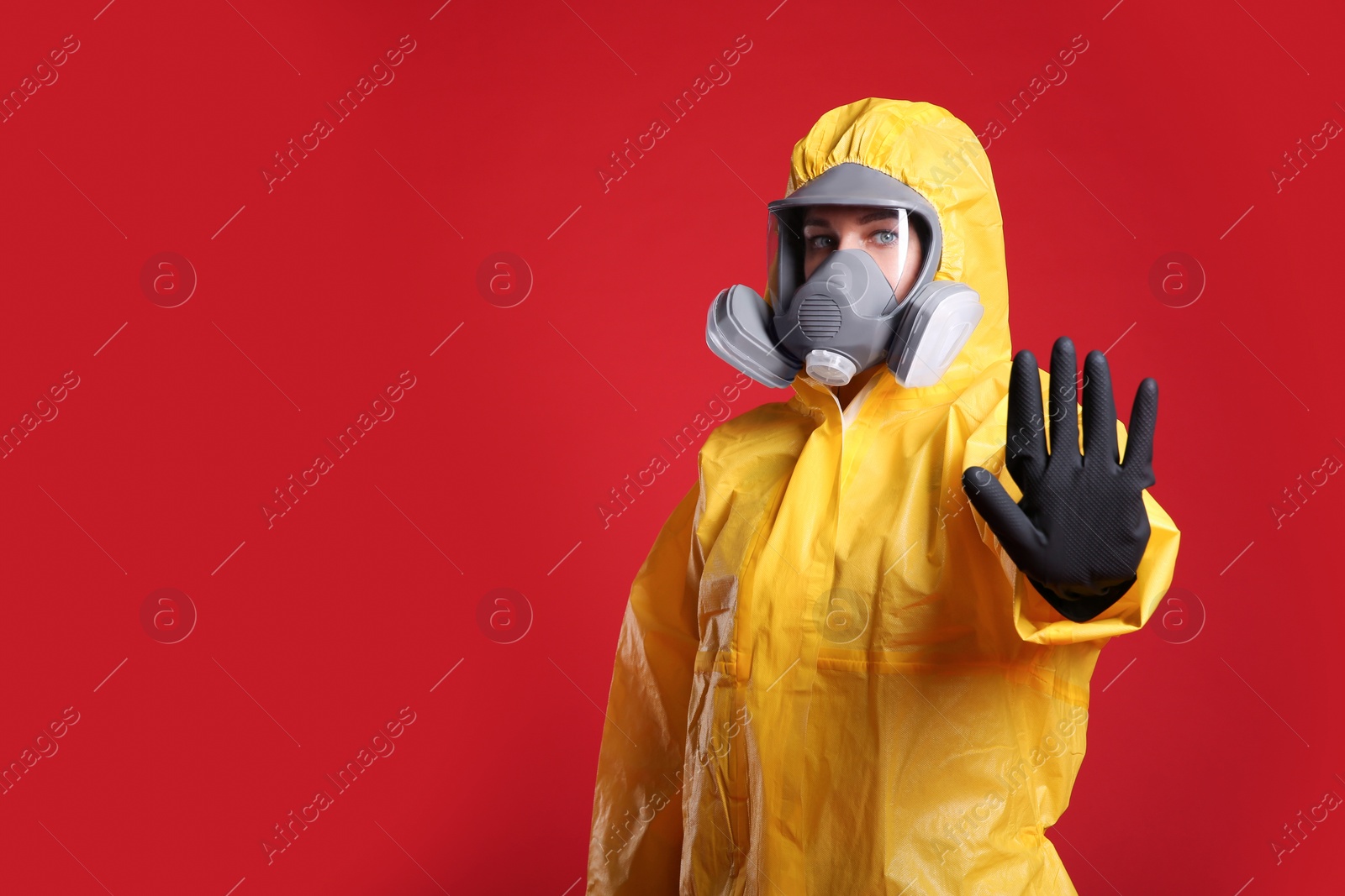 Photo of Woman in chemical protective suit making stop gesture on red background, space for text. Virus research