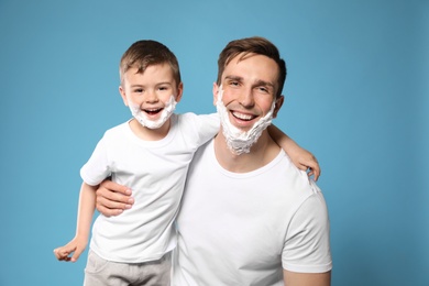 Photo of Dad and his little son with shaving foam on faces against color background