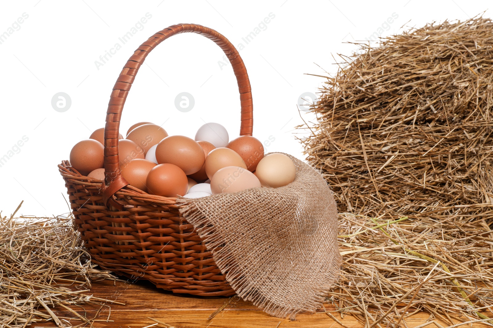 Photo of Wicker basket full of chicken eggs and dried straw on wooden table against white background