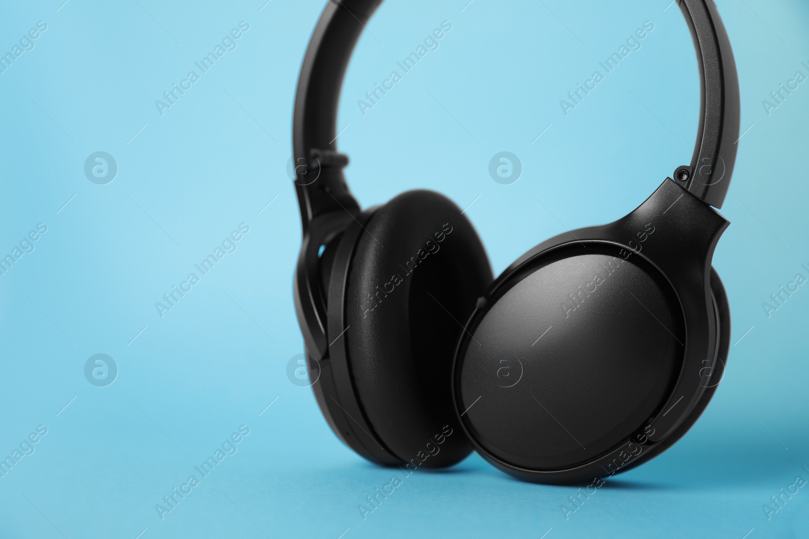 Photo of Modern wireless headphones on light blue background, closeup. Space for text