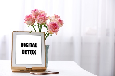 Photo of Tablet with phrase DIGITAL DETOX, smartphone and flowers indoors. Space for text