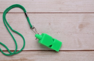 Photo of One green whistle with cord on light wooden table, top view. Space for text