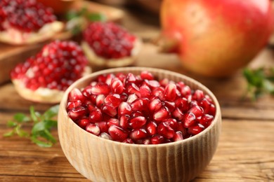 Photo of Delicious ripe pomegranate kernels in bowl on wooden table, closeup