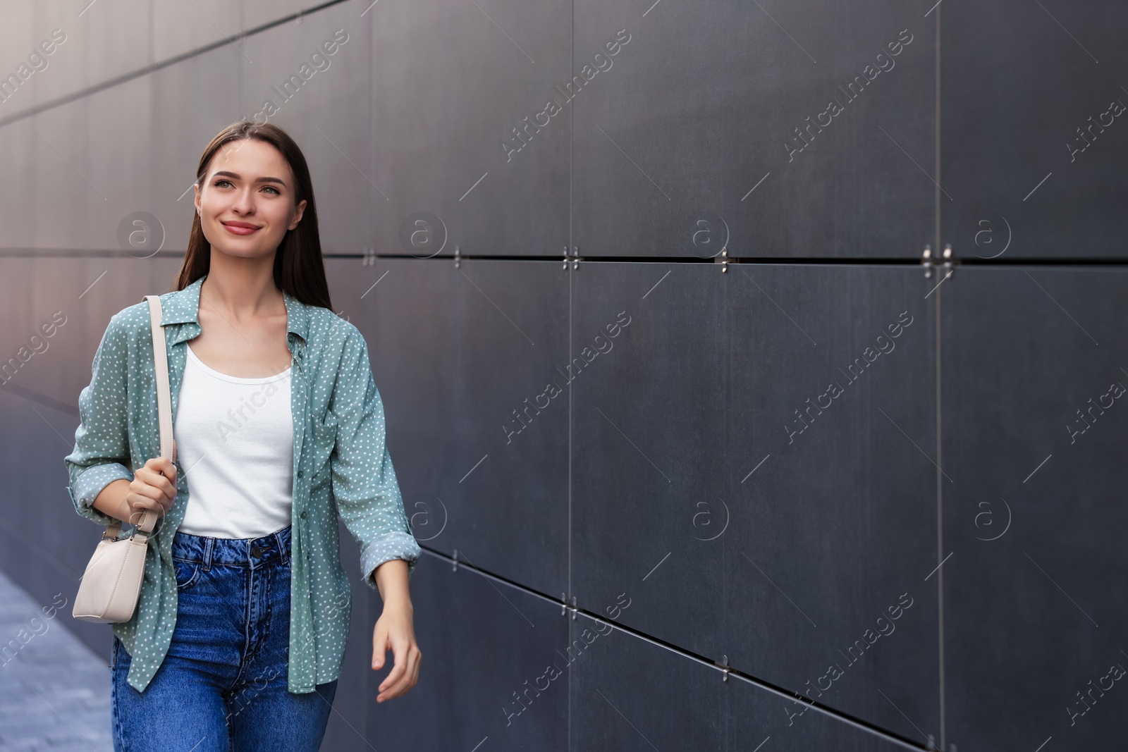 Photo of Young woman in casual clothes walking near grey wall outdoors, space for text