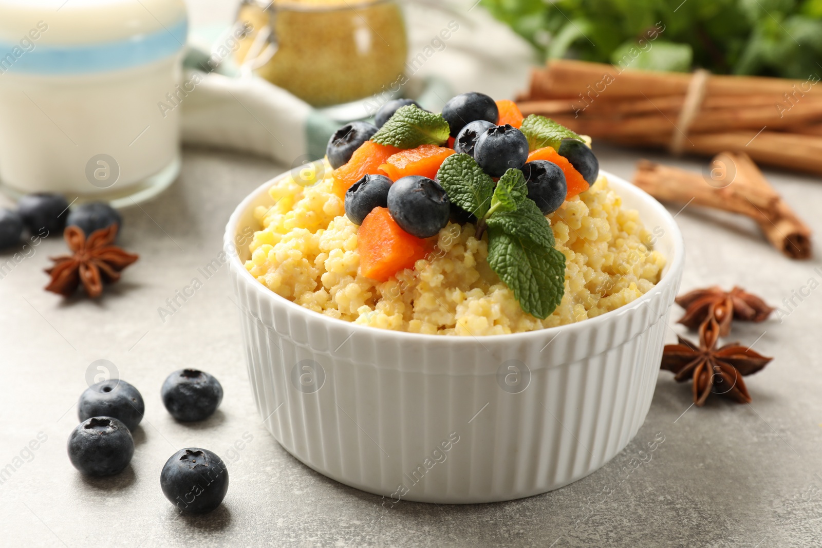 Photo of Tasty millet porridge with blueberries, pumpkin and mint in bowl on light grey table, closeup