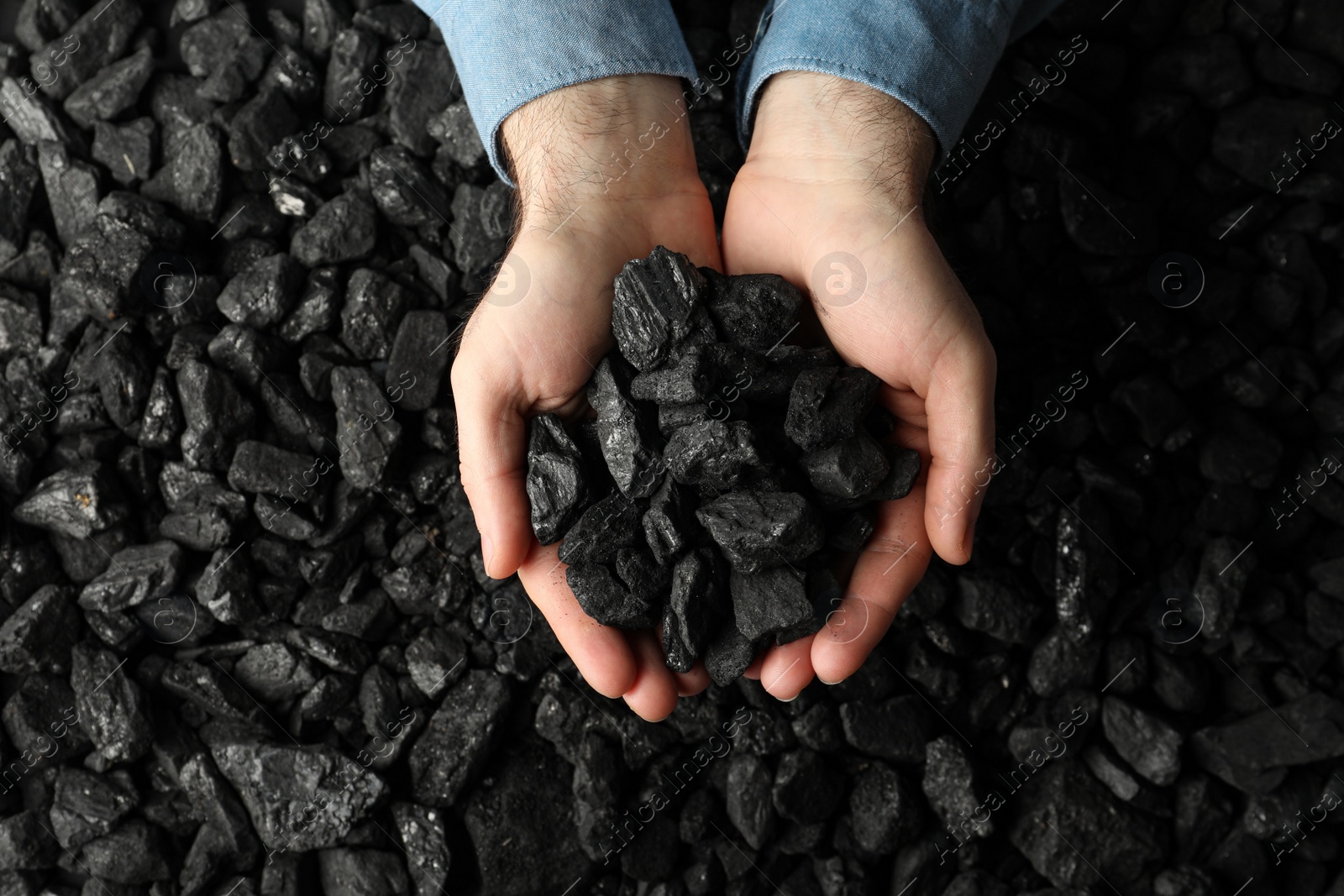 Photo of Man holding coal in hands over pile, top view