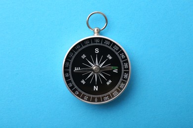 Photo of One compass on light blue background, top view. Tourist equipment