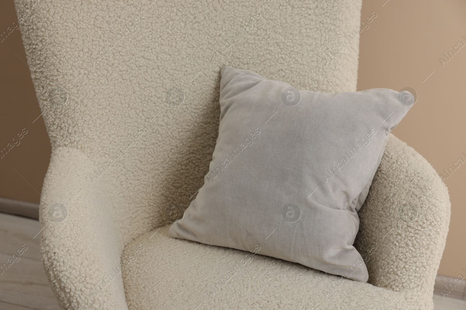Photo of Soft grey pillow on armchair near beige wall indoors