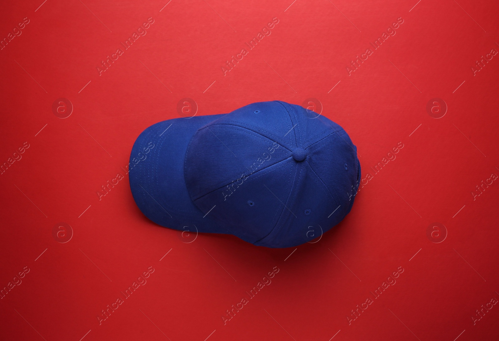 Photo of Stylish blue baseball cap on red background, top view