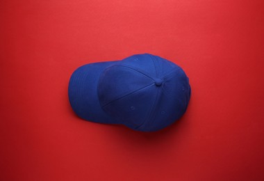 Photo of Stylish blue baseball cap on red background, top view