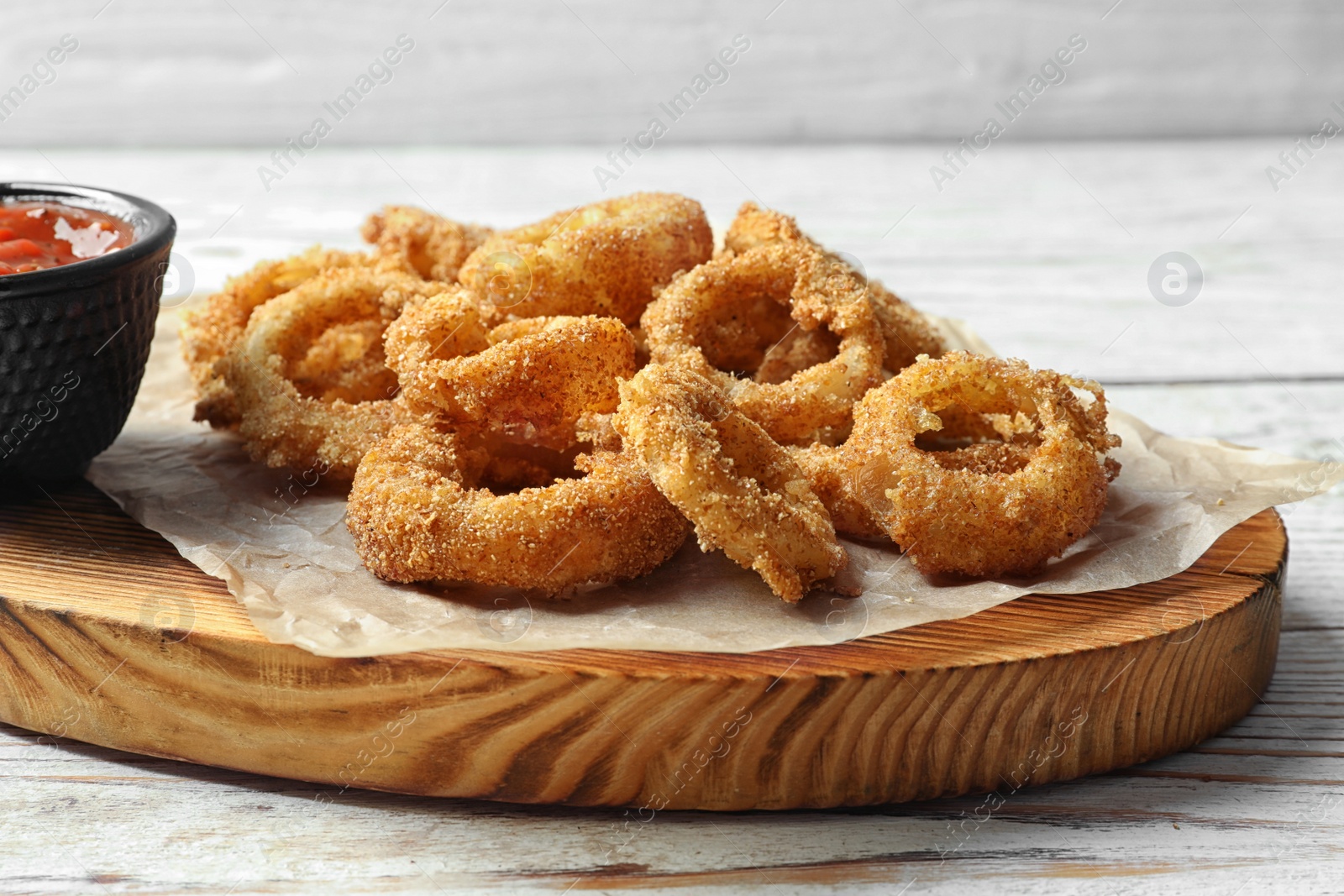 Photo of Homemade crunchy fried onion rings with tomato sauce on wooden table, closeup