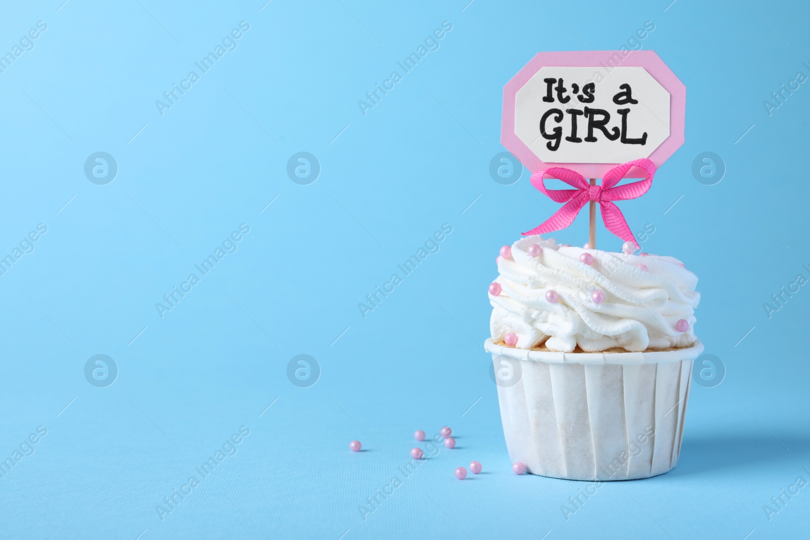 Photo of Beautifully decorated baby shower cupcake with cream and girl topper on light blue background. Space for text