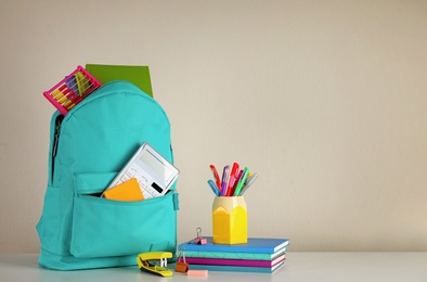Photo of Bright backpack and school stationery on table against light background, space for text