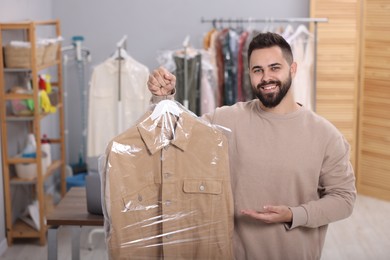 Dry-cleaning service. Happy man holding hanger with jacket in plastic bag indoors