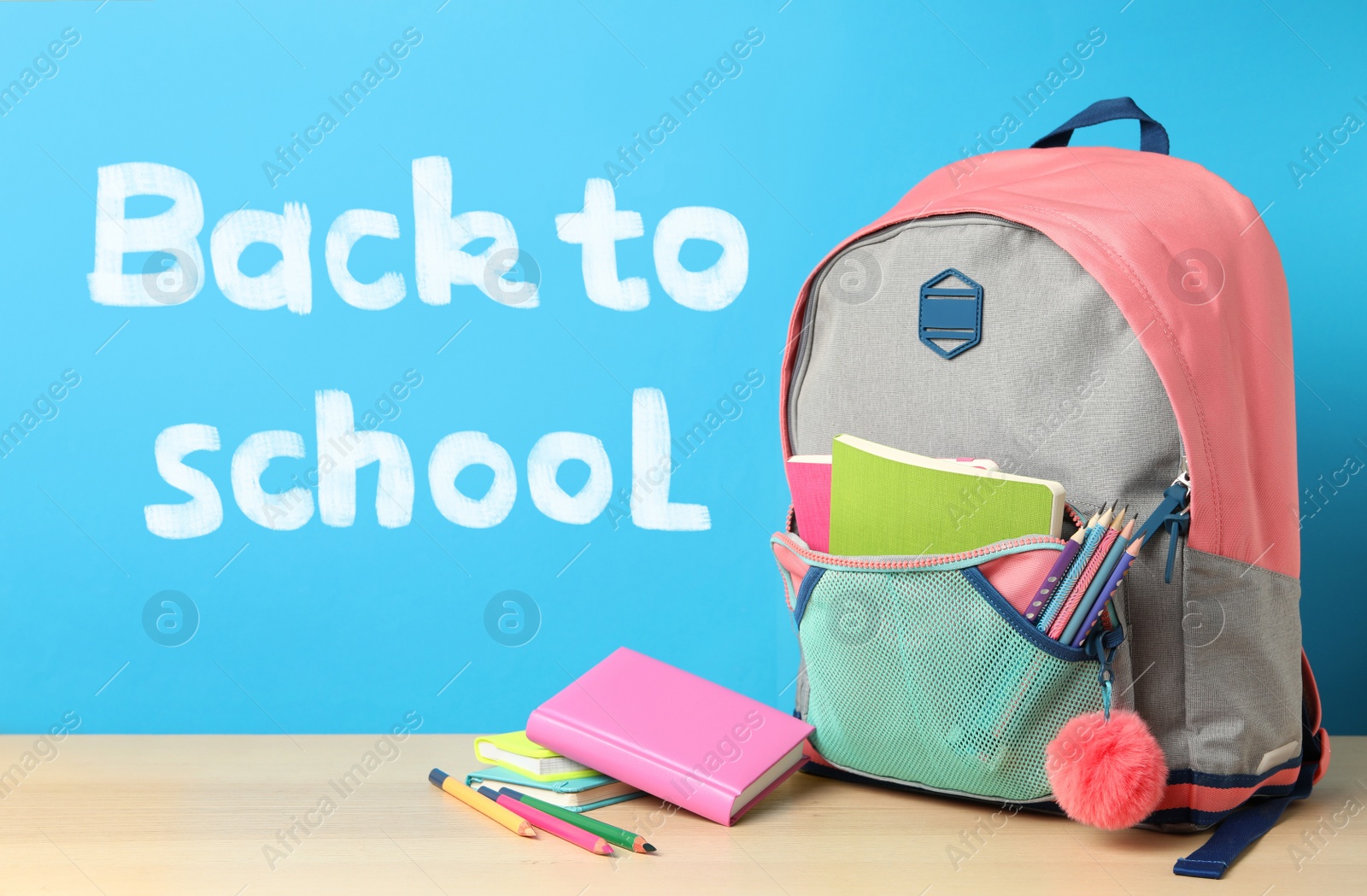 Image of Wooden table with backpack and stationery near text Back To School on blue background