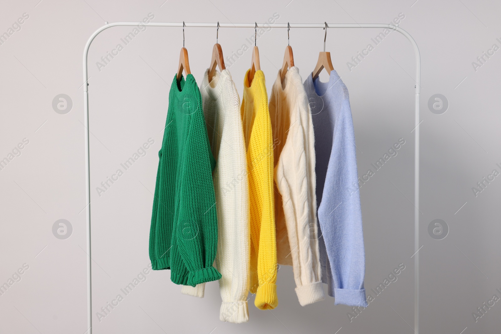 Photo of Rack with different warm sweaters on light background