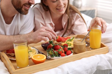 Photo of Happy couple eating tasty breakfast on bed, closeup