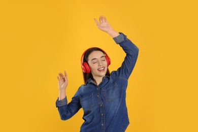Happy woman in headphones listening music and dancing on orange background