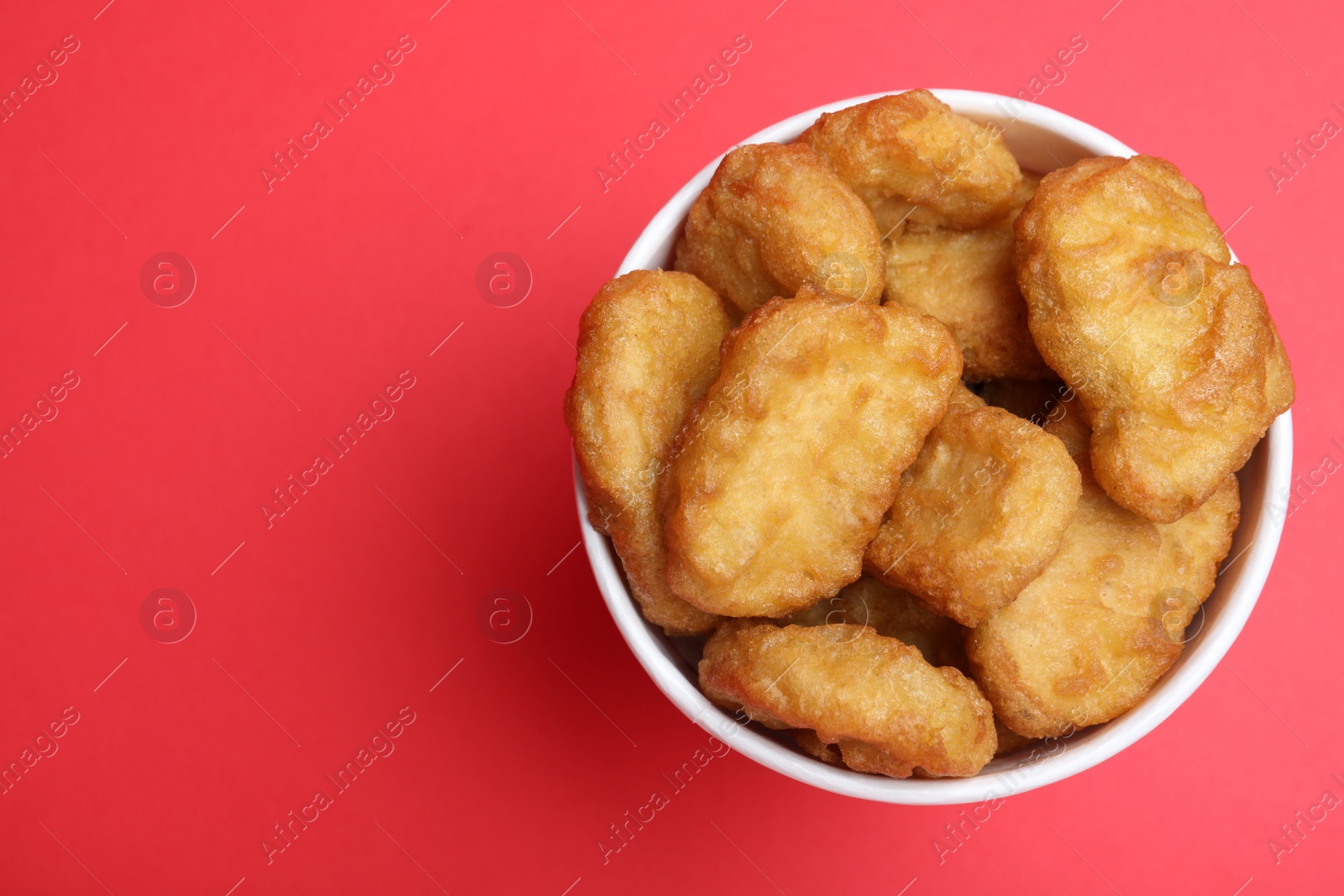 Photo of Bucket with delicious chicken nuggets on red background, top view. Space for text