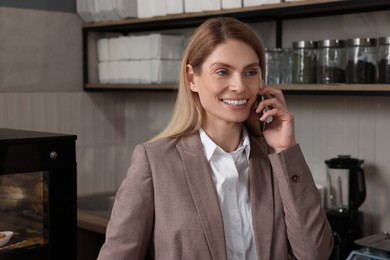 Photo of Happy business owner talking on phone in bakery shop