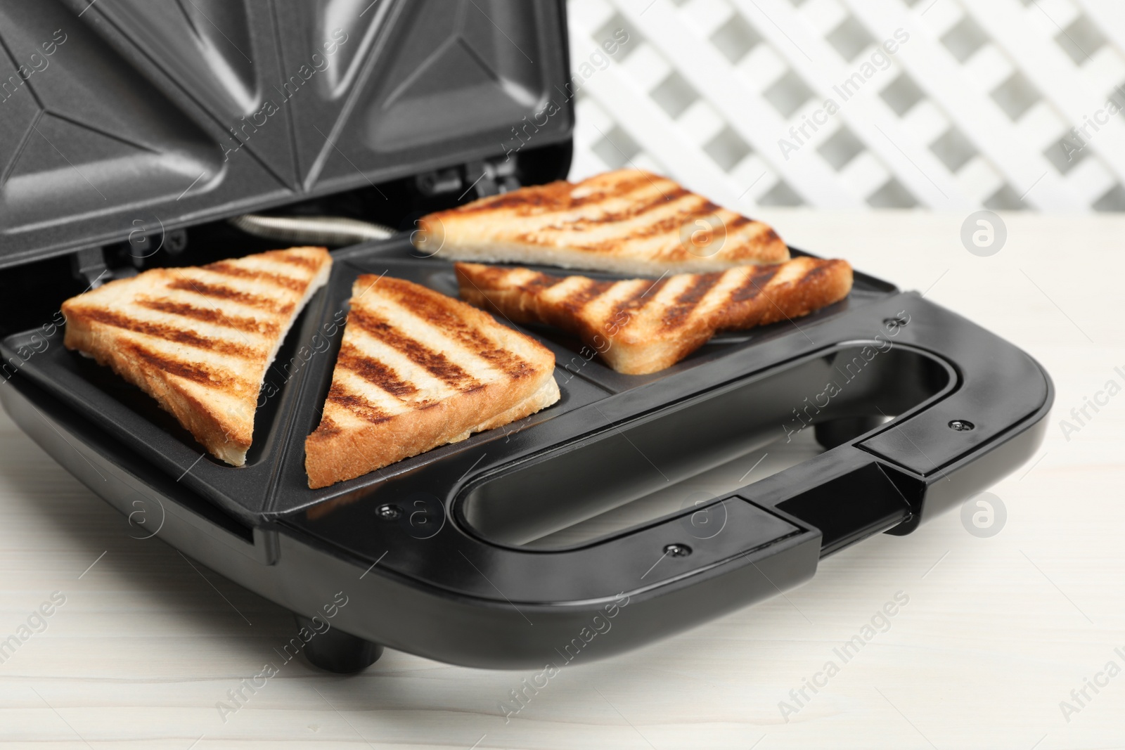 Photo of Modern sandwich maker with bread slices on white wooden table