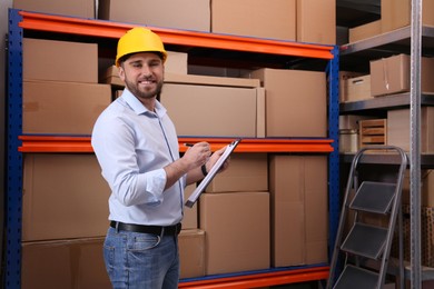 Young man with clipboard near rack of cardboard boxes at warehouse