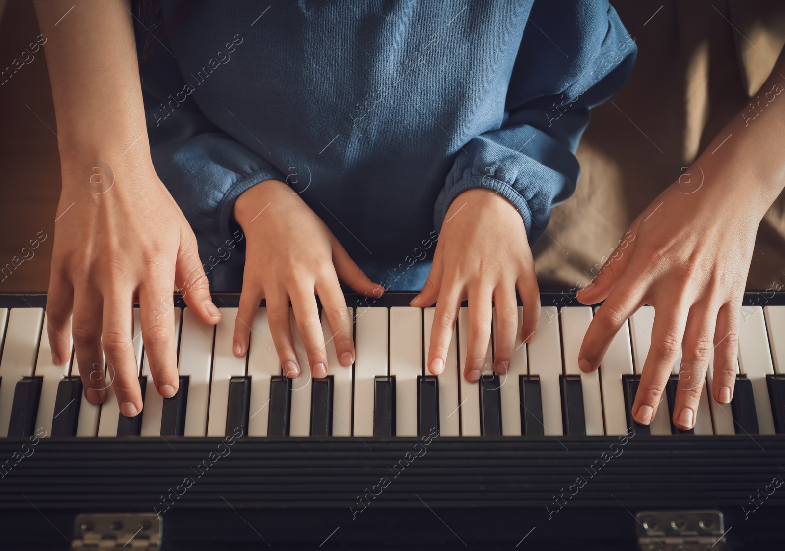 Photo of Young woman with child playing piano, above view. Music lesson