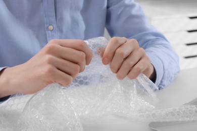 Photo of Woman popping bubble wrap at table in office, closeup. Stress relief