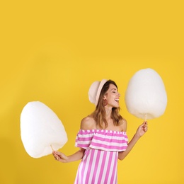 Photo of Happy young woman with cotton candies on yellow background