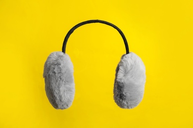 Fluffy earmuffs on yellow background. Stylish winter accessory