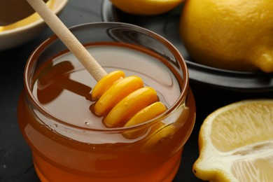 Photo of Sweet honey and fresh lemons on black table, closeup