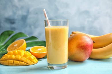 Photo of Glass of fresh mango drink and tropical fruits on table against color background