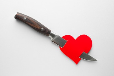 Photo of Red paper heart pierced with knife on white background, top view. Broken heart