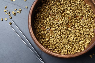 Photo of Bowl of gold nuggets and tweezers on black table, flat lay