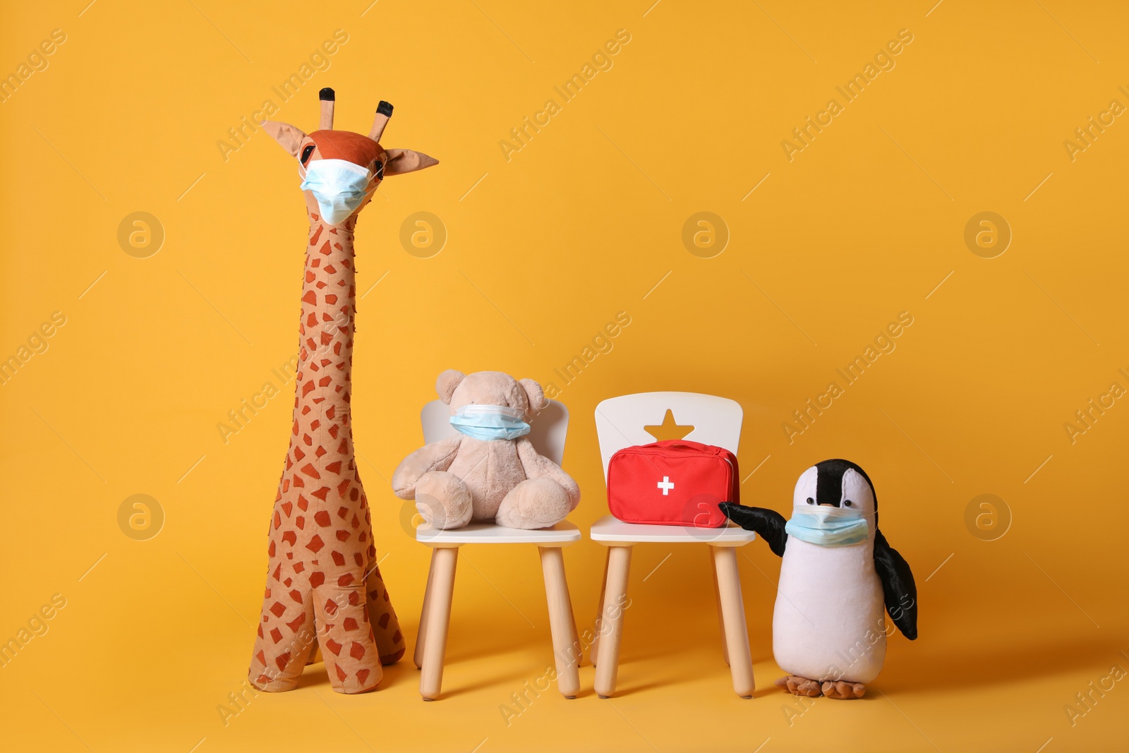 Photo of Toys with face masks and first aid bag on yellow background. Pediatrician practice
