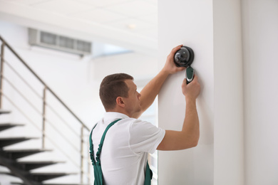 Technician installing CCTV camera on wall indoors