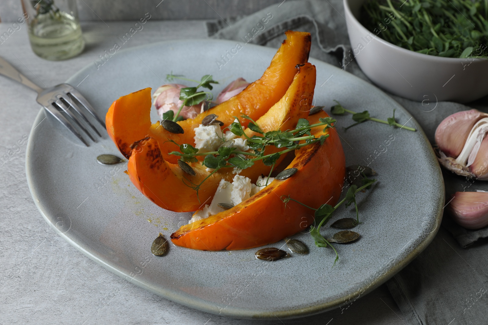 Photo of Baked pumpkin slices served with cheese, microgreens, seeds and garlic on light table, closeup