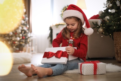 Photo of Cute little girl opening gift box in room decorated for Christmas