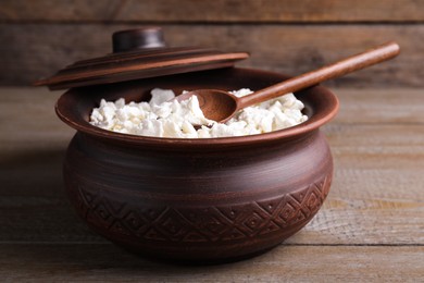 Photo of Clay pot with cottage cheese and spoon on grey wooden table