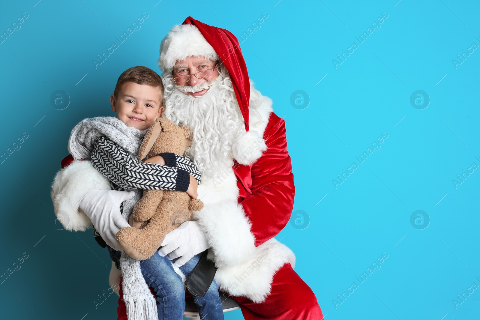 Photo of Little boy with toy bunny sitting on authentic Santa Claus' lap against color background