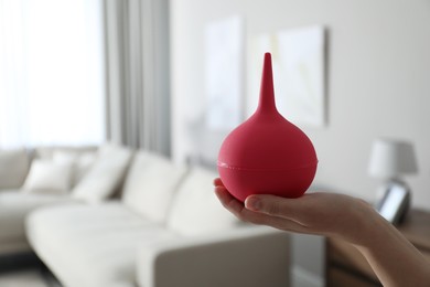 Woman holding pink enema at home, closeup. Space for text