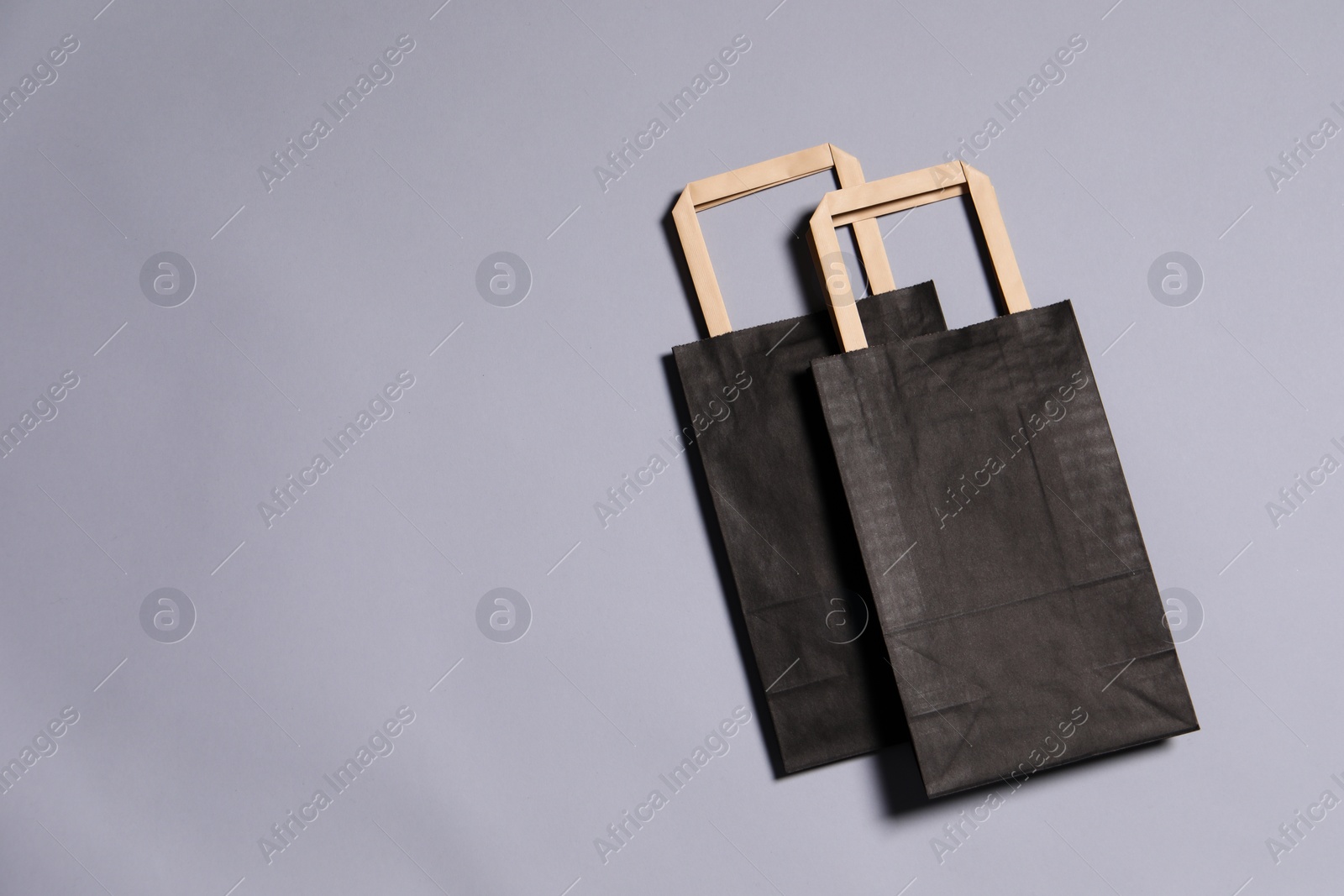 Photo of Two black paper shopping bags on grey background, top view. Space for text