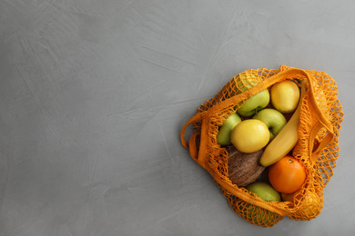 Photo of Net bag with fruits on light grey table, top view. Space for text