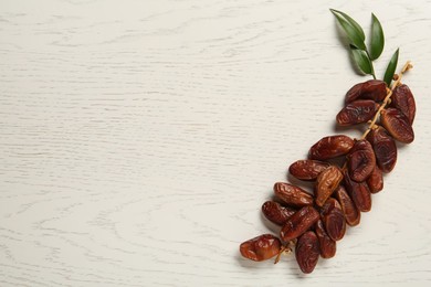 Photo of Branch of sweet dried dates and green leaves on white wooden table, top view. Space for text