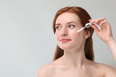 Photo of Beautiful woman with freckles applying cosmetic serum onto her face against grey background. Space for text