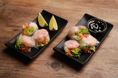Photo of Tasty spring rolls served with lime and soy sauce on wooden table