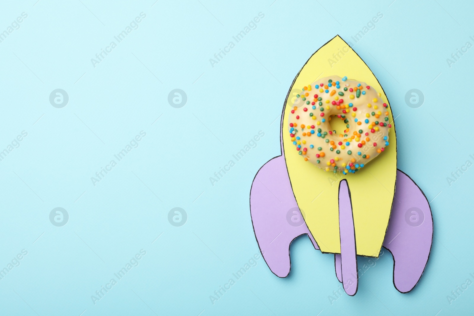 Photo of Rocket made with donut and paper on light blue background, top view. Space for text