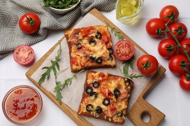 Tasty pizza toasts and ingredients on white tiled table, flat lay