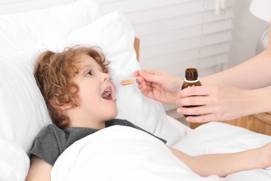 Photo of Mother giving cough syrup to her son on bed indoors, closeup